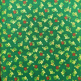A folded piece of green fabric with a small repeating floral print in yellow, red, and white, laid flat on a brown wooden surface.