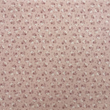 A folded piece of fabric with a dense small floral print in muted pink and green on an off-white background, laid flat on a dark wood surface.