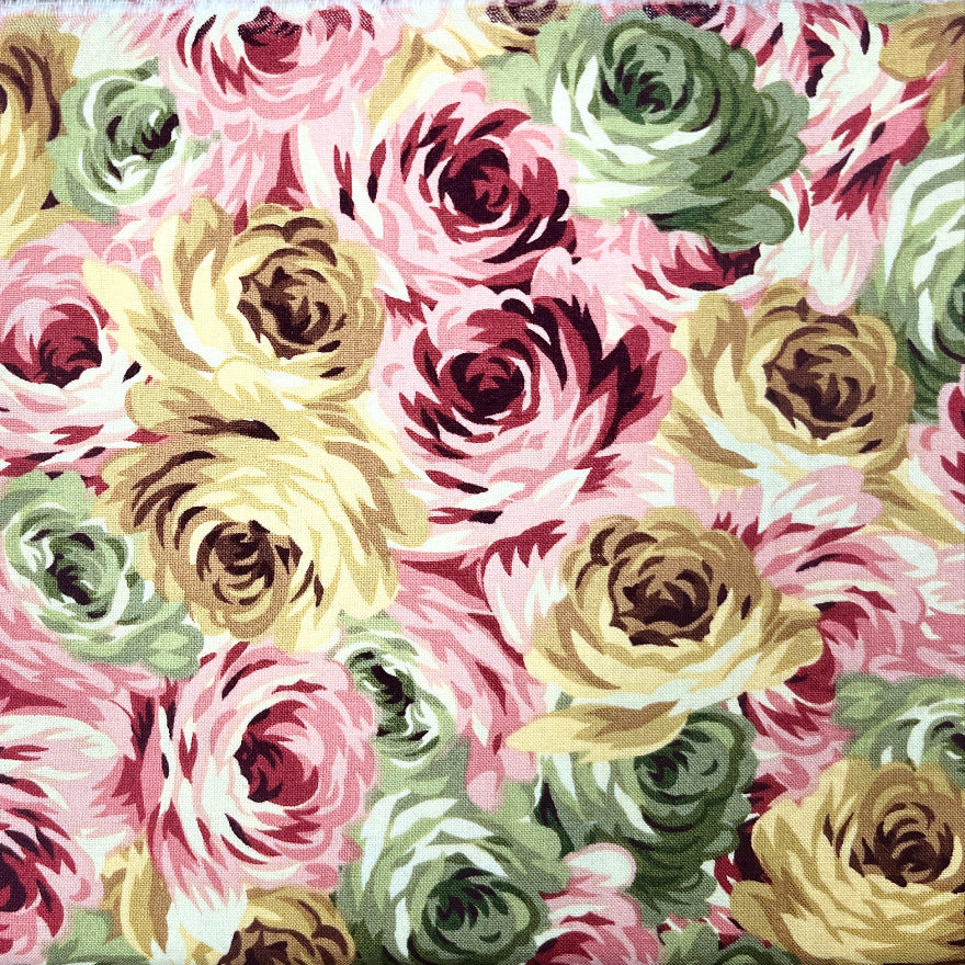 A rectangular fabric sample with a dense floral print of large roses in pink, cream, olive green, and burgundy, laid flat on a dark wood floor.