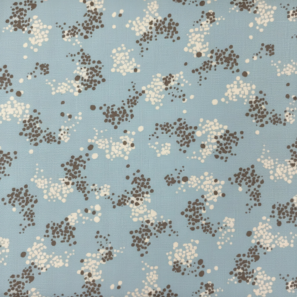 A light blue fabric with a brown and cream floral pattern, laid flat on a dark brown wooden surface.