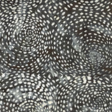 A close-up of a black fabric or material featuring a white dotted spiral pattern, with a blurred brown textured surface visible above it.