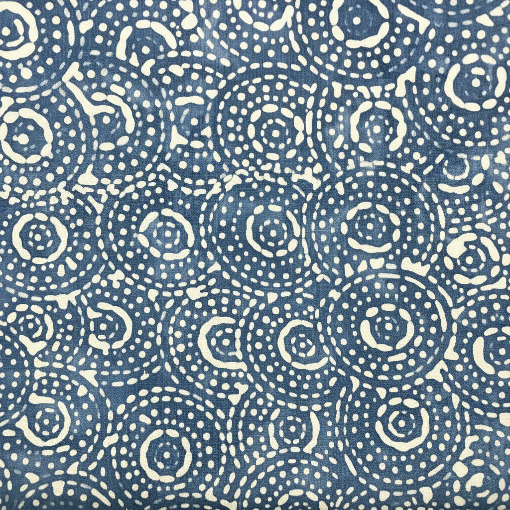 A hand holding a folded fabric panel with a navy blue and white circular dot pattern, layered over other colorful patterned fabrics.