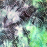 A close-up of a patterned fabric or material being held up by a hand. The surface has an abstract design with swirling marbled areas in black, green, purple, and white, overlaid with dotted circular motifs.