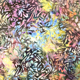 A close-up of a folded piece of batik fabric with a dense, abstract leaf-like pattern in a multicolor mix of purple, blue, yellow, pink, and black, held by a hand.