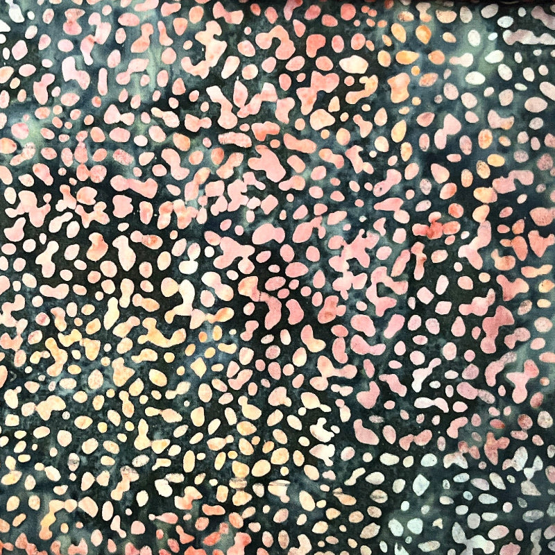 A close-up of a person's hand lifting a dark patterned fabric cover to reveal colorful patterned fabrics underneath stacked on a table.