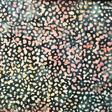 A close-up of a person's hand lifting a dark patterned fabric cover to reveal colorful patterned fabrics underneath stacked on a table.
