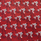 A close-up of a folded red fabric, likely cotton block-printed cotton fabric, featuring a repeating white and dark brown floral or paisley pattern.