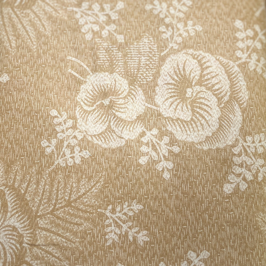A close-up of a beige fabric table runner with a white floral pattern, laid out on a dark wooden table.