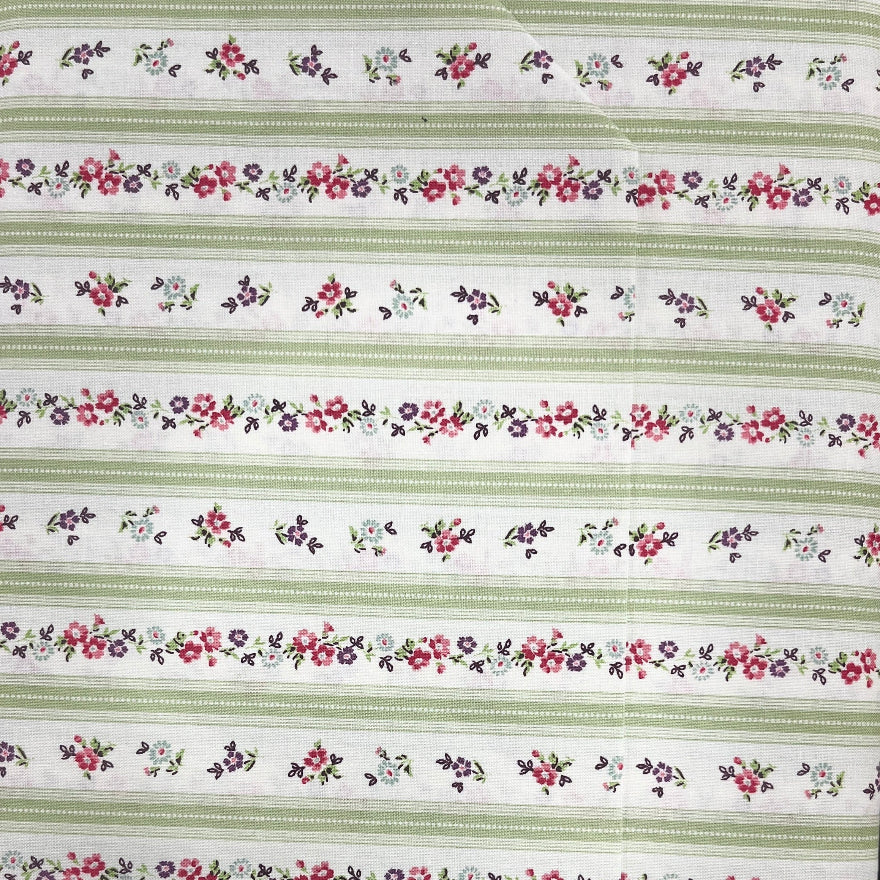 A close-up of a striped fabric or wallpaper pattern featuring horizontal bands of green, white, and red floral motifs, held by a hand.