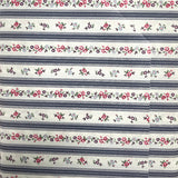 A close-up of a fabric item, likely a bed sheet or pillowcase, featuring a repeating horizontal pattern of navy blue stripes and delicate floral garlands in pink, red, and green on a white background.