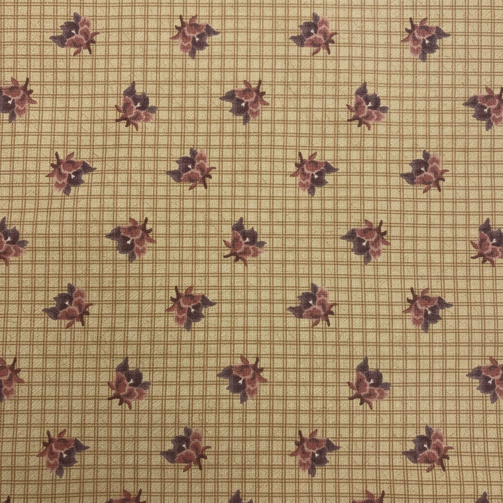 A close-up of a beige necktie featuring a fine grid pattern and a repeating dark floral motif, held by a hand.