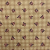 A close-up of a beige necktie featuring a fine grid pattern and a repeating dark floral motif, held by a hand.