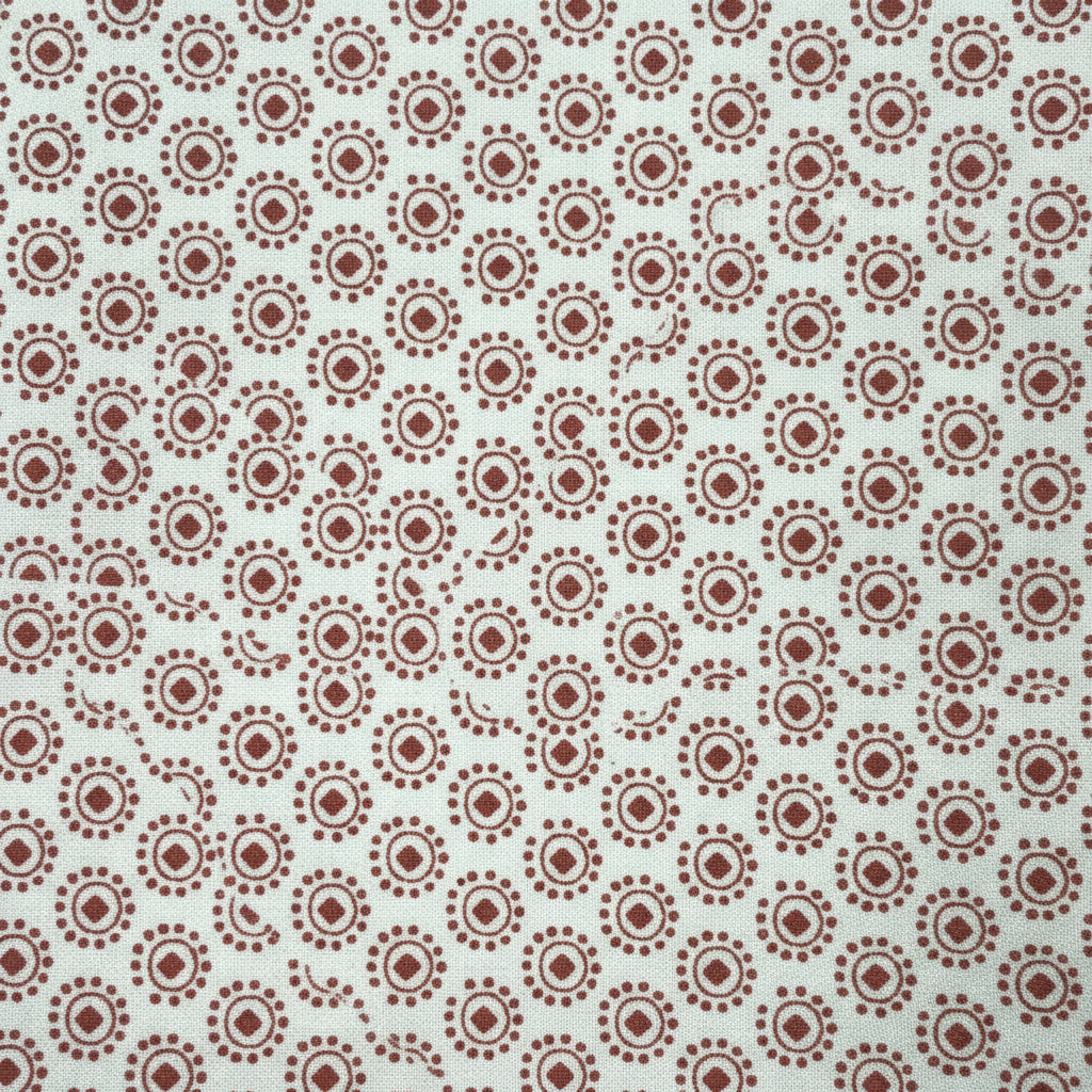 A close-up of a white fabric or paper material printed with a repeating brown circular floral/dot pattern, with a yellow patterned edge visible on the right side.