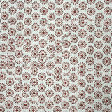 A close-up of a white fabric or paper material printed with a repeating brown circular floral/dot pattern, with a yellow patterned edge visible on the right side.