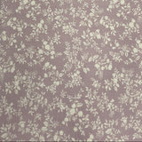 A close-up of a fabric or material sample with a small-scale floral pattern in cream on a muted dusty lavender-gray background, laid flat on a dark wooden surface.