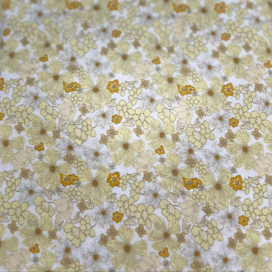 A close-up of a fabric or material sample with a repeating floral pattern in pale yellow, white, and muted gold tones.