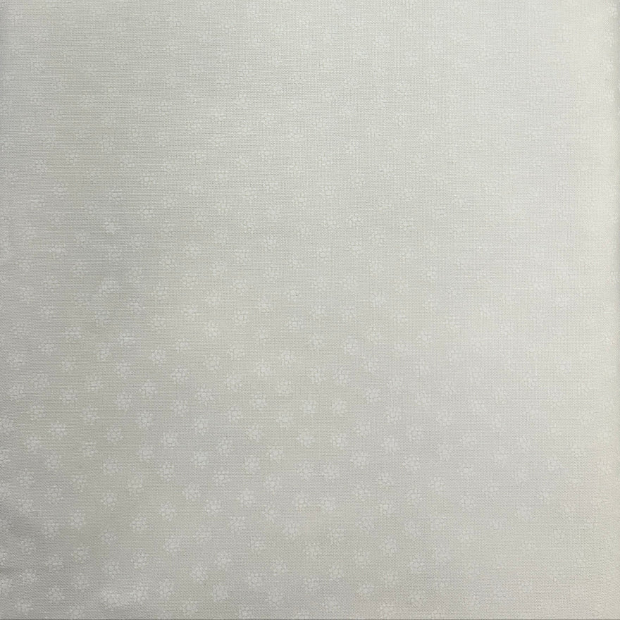 A close-up of a white textured fabric or foam panel with a subtle dotted pattern, held up against a dark wooden table background.