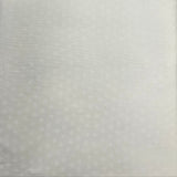 A close-up of a white textured fabric or foam panel with a subtle dotted pattern, held up against a dark wooden table background.