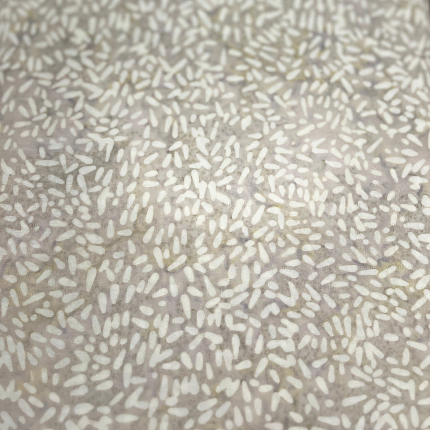 A close-up of a textured surface with a dense speckled pattern of small beige, white, and light brown dashes on a warm taupe-beige background.