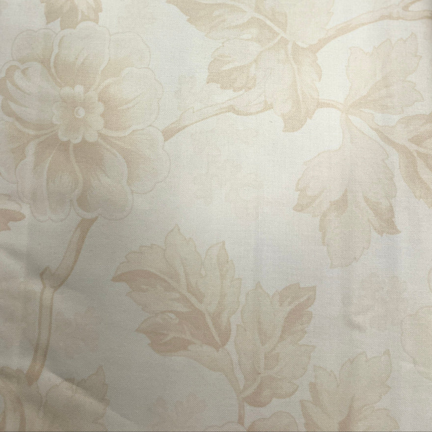 A close-up of a beige floral patterned fabric, likely upholstery or wallpaper, draped vertically. The fabric features a raised, tonal floral motif on a warm cream background.
