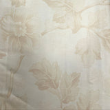 A close-up of a beige floral patterned fabric, likely upholstery or wallpaper, draped vertically. The fabric features a raised, tonal floral motif on a warm cream background.