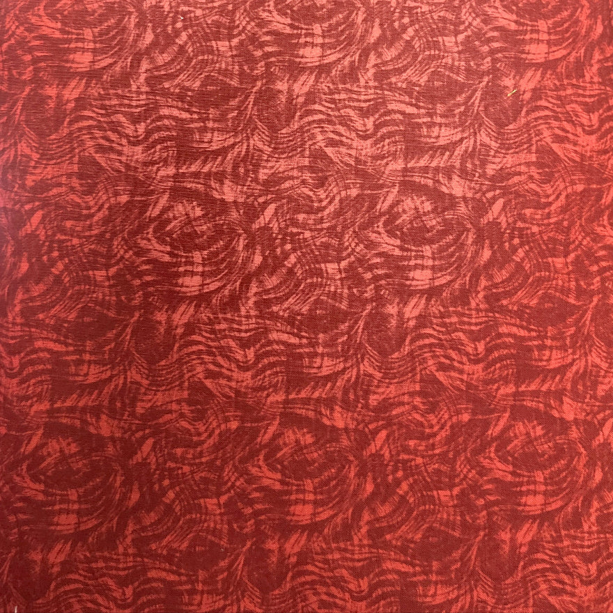 A close-up of a red textured material with an abstract wavy pattern, shown standing vertically with a blurred indoor background.
