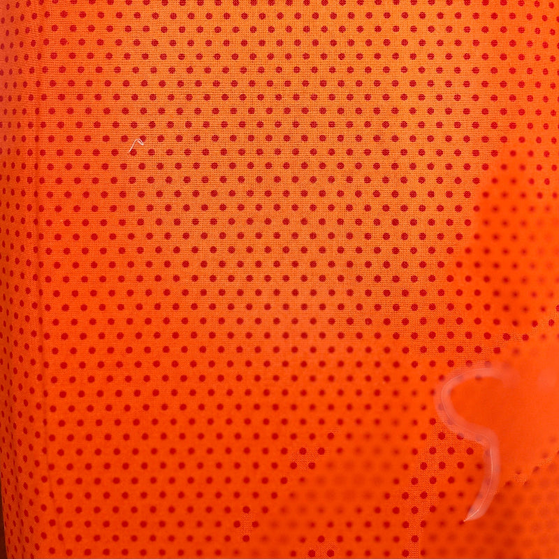 Close-up of a bright orange perforated fabric or mesh material with a small repeating hole pattern, photographed indoors with some surrounding objects visible at the edges.
