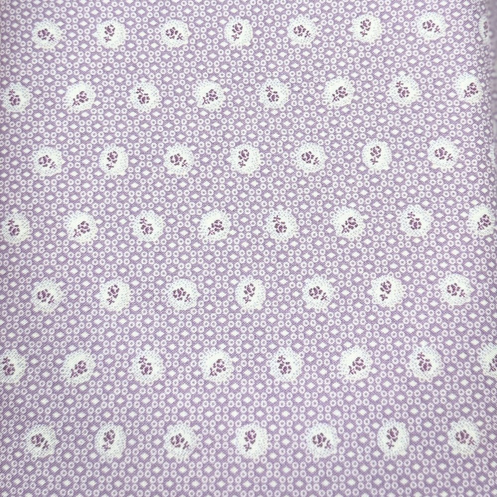 A close-up of a lavender-purple fabric with a repeating small white floral or paisley-like dot pattern, next to a pink patterned fabric strip.