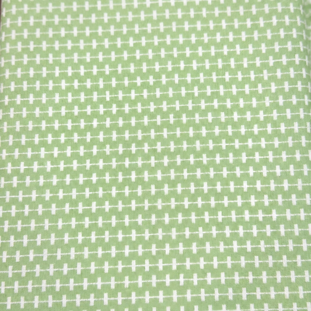 A close-up of a fabric or wallpaper pattern featuring a repeating white cross-hatch grid on a muted sage green background.