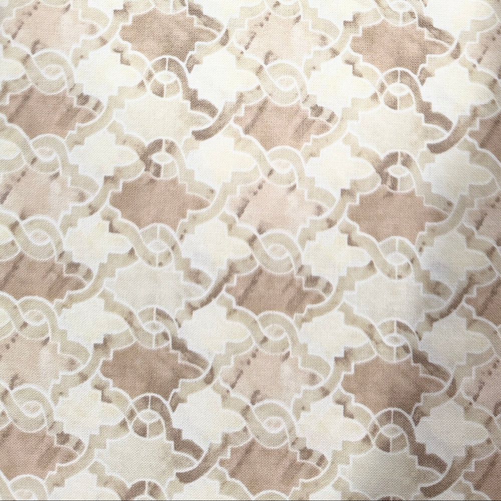 A close-up of a beige and cream patterned fabric or wallpaper sample with a repeating geometric floral design, held by a hand on the right side.