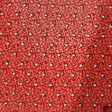 A close-up of a red patterned fabric or wallpaper sample featuring a small repeating floral or starburst motif in white, black, and yellow.