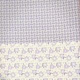 A folded piece of patterned fabric or paper showing two distinct printed sections: a top section with dense small gray-blue text and a bottom section with a repeating light purple floral or medallion pattern on a white background.