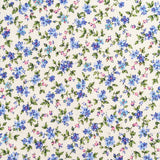 A close-up of a fabric yardage with a dense small floral print in blue, purple, and green on a cream background, held at the bottom by a hand. Other floral fabrics are partially visible on either side.