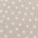 A close-up of a beige fabric or material sample with a repeating small floral pattern, held flat against a wooden surface. A purple stitched edge is visible along the right side, and another patterned fabric strip appears at the far right edge.