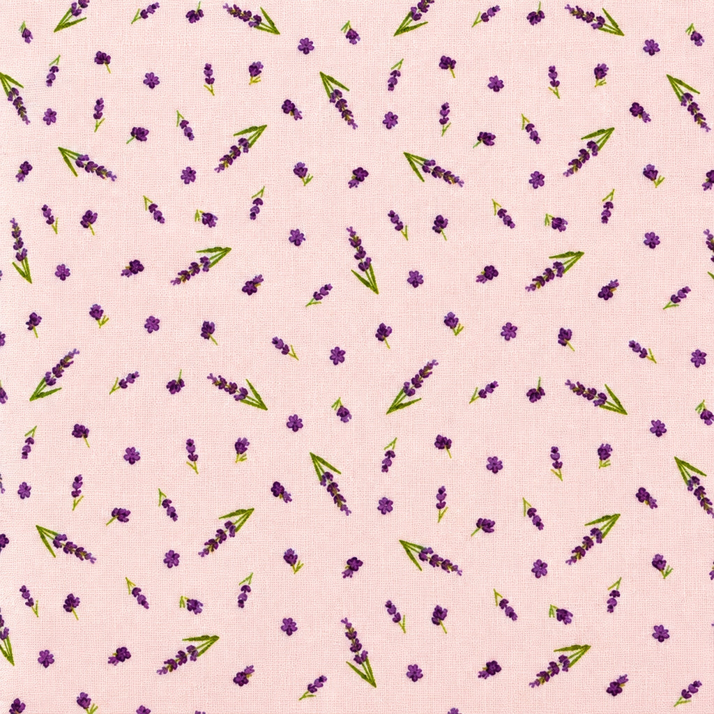 A close-up of a light pink fabric with a repeating pattern of small purple flowers and green leaves, laid flat next to other fabrics.