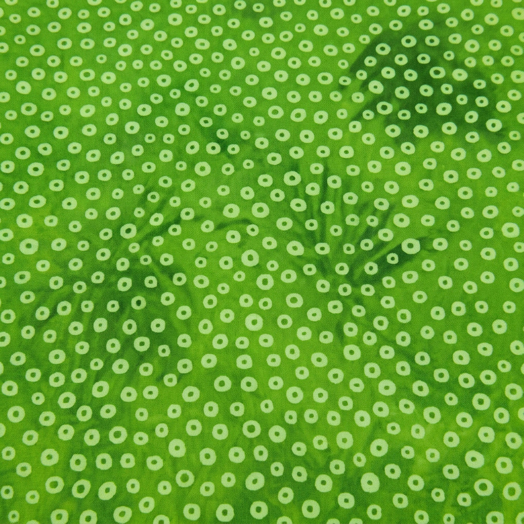 A close-up of a green fabric yardage with a white ditsy floral print, held down by a hand on a wooden table.