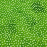A close-up of a green fabric yardage with a white ditsy floral print, held down by a hand on a wooden table.