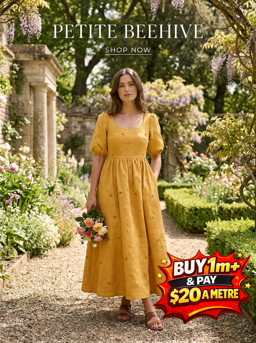 Woman in a butterscotch yellow Petite Beehive dress with puffed sleeves and textured bee embroidery, holding flowers.