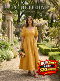 Woman in a butterscotch yellow Petite Beehive dress with puffed sleeves and textured bee embroidery, holding flowers.