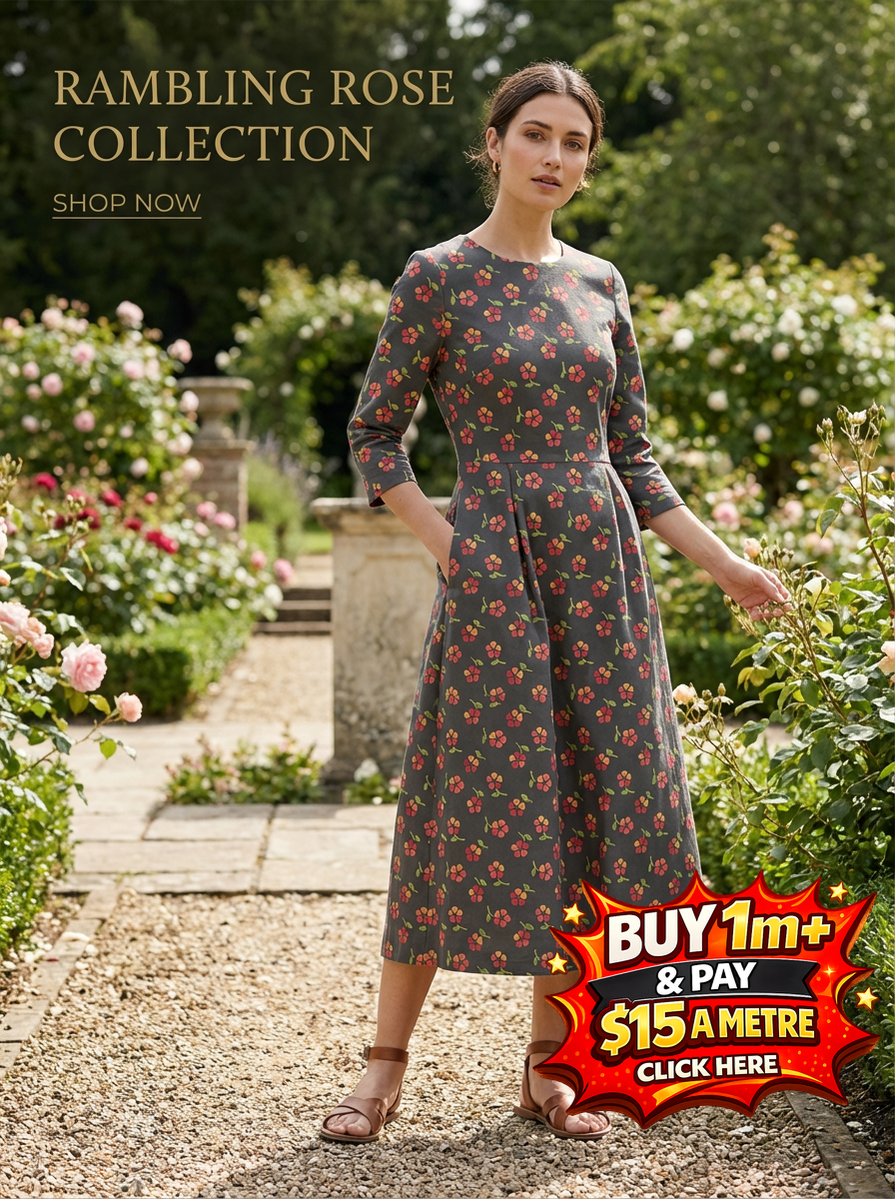 Woman in a grey Rambling Rose floral print dress with 3/4 sleeves, standing in a rose garden.
