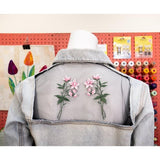 Light blue denim jacket with two pink floral embroidery designs on a sheer back panel.
