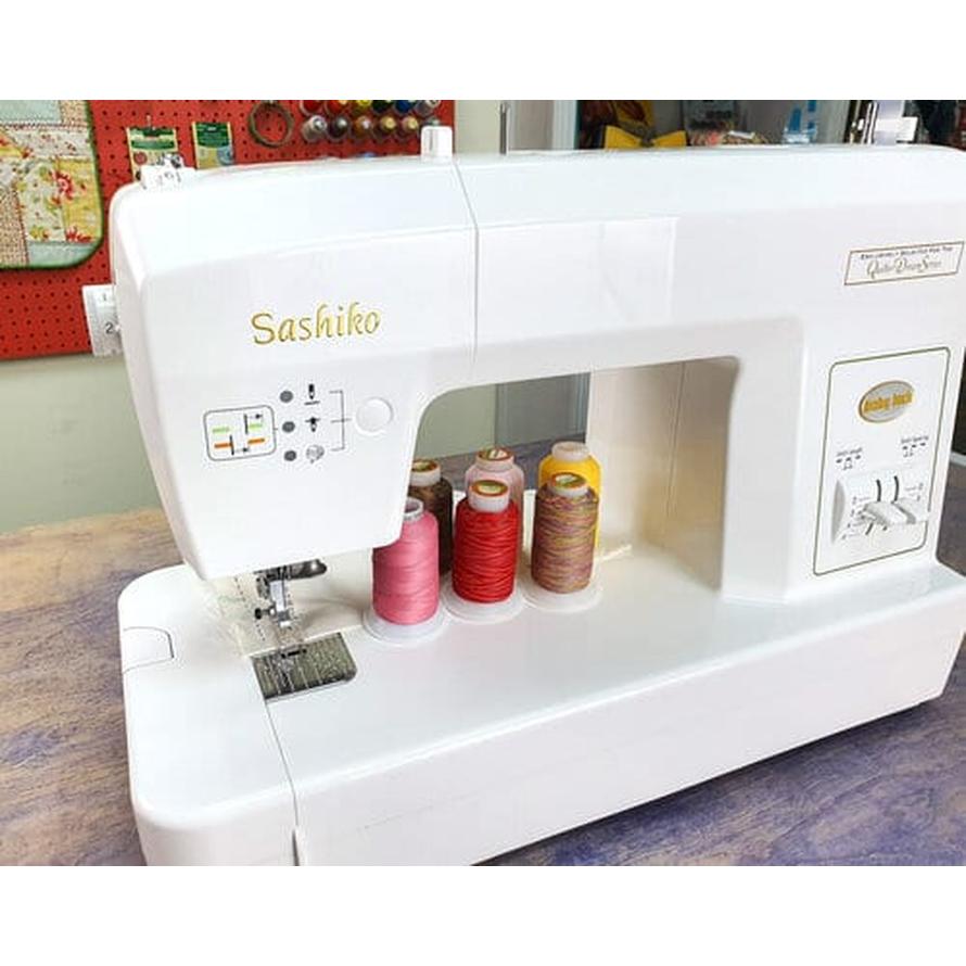 White Sashiko sewing machine with four spools of Silco lint-free cotton thread in orange, rust, yellow, and pink.