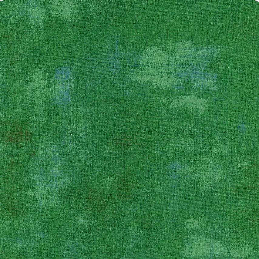 A square fabric or material swatch in mottled green tones with a subtle grid texture and a small ruler scale along the bottom edge.