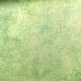 A close-up of textured fabric in a mottled sage green and light yellow-green colorway, with a folded section showing the material's depth and weave.